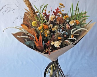 May include: A bouquet of dried flowers in shades of brown, orange, and yellow, wrapped in brown paper and tied with a black ribbon.