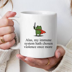May include: White ceramic mug featuring a cartoon frog wearing a cape and holding a knife. The mug has the text "Alas, my immune system hath chosen violence once more".