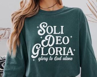 May include: A teal sweatshirt featuring the white text "SOLI DEO GLORIA" and "glory to God alone". The long-sleeved, crew neck top is a comfortable style. The image also shows the colours "Comfort Colors Blue Spruce".