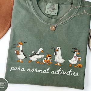 Peut inclure: T-shirt vert Comfort Colors avec un motif sur le thème d'Halloween. Le motif représente des oies de dessin animé déguisées en analyste de données, une oie qui court, une citrouille, un fantôme et une sorcière. Le texte "para normal activities" est en dessous.