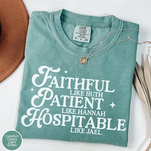 May include: A light green Comfort Colors t-shirt with the words "Faithful Like Ruth, Patient Like Hannah, Hospitable Like Jael" in white script. A gold necklace with a pendant is on the shirt. The shirt is size S-P-CH.