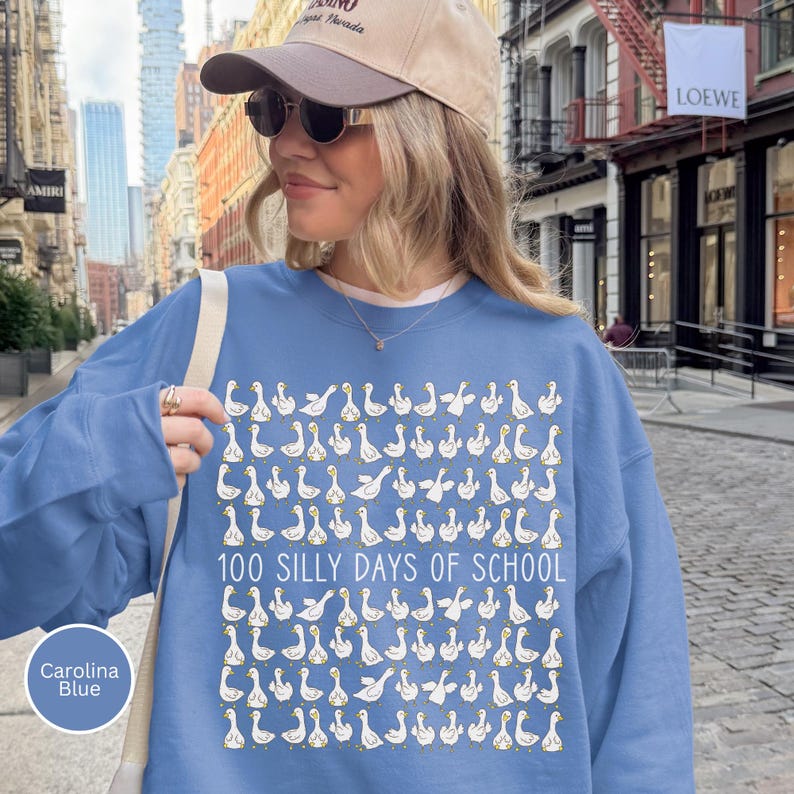 K&ouml;nnte beinhalten: Carolina-Blaues Sweatshirt mit wei&szlig;em G&auml;nsemuster und dem Text "100 SILLY DAYS OF SCHOOL". Das Sweatshirt hat einen Rundhalsausschnitt.