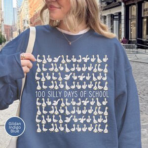 K&ouml;nnte beinhalten: Indigoblaues Sweatshirt mit einem Muster aus wei&szlig;en G&auml;nsen und dem Text "100 SILLY DAYS OF SCHOOL". Das Sweatshirt besteht aus einem weichen Material, ideal f&uuml;r die Schule.