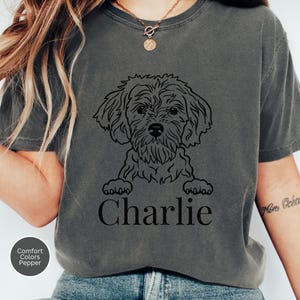May include: Dark grey t-shirt featuring a black line drawing of a dog with the name "Charlie" printed below. The shirt has a crew neck and short sleeves. The Comfort Colors brand and Pepper color are noted on the bottom left.