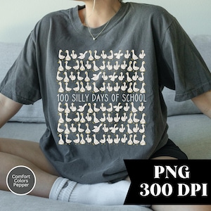 May include: Dark gray t-shirt featuring a repeating pattern of cartoon geese with yellow beaks and feet. The text "100 SILLY DAYS OF SCHOOL" is printed in white. The shirt is a Comfort Colors Pepper brand.