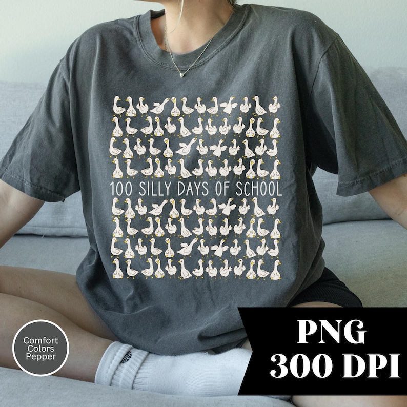 May include: Dark gray t-shirt featuring a repeating pattern of cartoon geese with yellow beaks and feet. The text "100 SILLY DAYS OF SCHOOL" is printed in white. The shirt is a Comfort Colors Pepper brand.