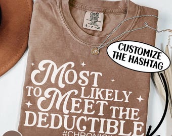 Könnte beinhalten: Espressofarbenes T-Shirt mit dem weißen Text "Most Likely to Meet the Deductible". Das Shirt hat auch den Hashtag #CHRONICILLNESS. Eine silberne Halskette mit Anhänger liegt über dem Shirt.