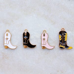 May include: Four colourful cowboy boot charms. The boots are white, black, pink, and black with yellow accents. Each boot has a gold-coloured top loop and a star design. The boots are approximately 2.5 cm in height.