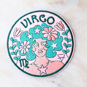 以下が含まれることがあります： 乙女座の星座デザインが施された刺繍パッチ。 ターコイズ色の髪、花、星を持つ女性の顔がピンク色の背景に描かれています。「VIRGO」の文字は緑色で、緑色の縁取りがされています。