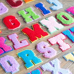 Op de afbeelding: Een set kleurrijke viltletters in verschillende kleuren, waaronder roze, blauw, groen, geel en rood. De letters zijn alfabetisch gerangschikt en zijn perfect voor knutselprojecten of decoratie.