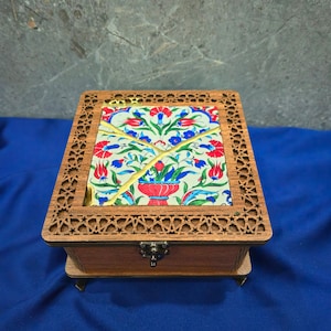 May include: A square wooden box featuring a laser-cut geometric lattice border and a central ceramic tile inlay. The tile displays a colorful floral pattern of red tulips and blue blossoms, accented by a gold-colored kintsugi-style crack design.