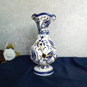 Op de afbeelding: Een wit en blauw keramieken vaas met een bloemenontwerp. De vaas heeft een bolvormig lichaam en een uitlopende, gerimpelde rand. De vaas is gerepareerd met goudkleurige kintsugi. De vaas is ongeveer 25 cm hoog.