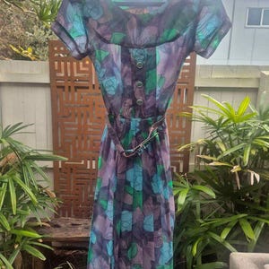 May include: A vintage floral print dress with a scoop neck, short sleeves, and a belt. The dress is made of a lightweight fabric and has a flowing silhouette. The print features blue, green, and purple flowers on a dark background.