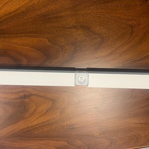 May include: A close-up of a white wall mounted light fixture with a small, square, clear plastic cover over the light bulb.