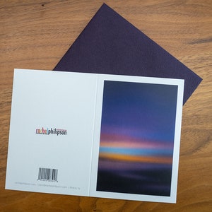 May include: A blank greeting card with a purple sunset photo on the front. The back of the card has a barcode and the text "rachelphilpson.com | rachelphilpson.com | Press TV".