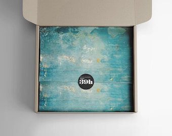 May include: A cardboard box with a blue and white patterned paper inside. The paper has a black circle sticker with the text "Rachel Purser Studio 39h" on it.