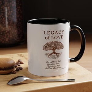 May include: White ceramic mug with a black interior and handle. The mug features the text "LEGACY of LOVE" and a tree graphic. Additional text includes "Faith, Love, Integrity, Wisdom" and a Bible verse.