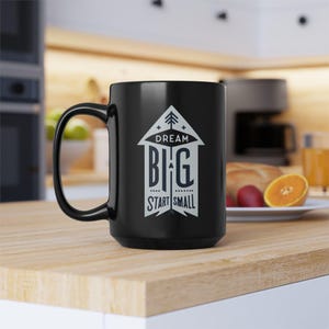 May include: Black ceramic coffee mug with a white graphic design that reads "Dream Big Start Small" with a stylized arrow pointing upwards.