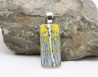 May include: A silver pendant necklace with a rectangular glass charm featuring a painted scene of birch trees with yellow and gray leaves.