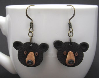 May include: A pair of handmade bear earrings. Each earring features a black bear face with brown eyes, a tan snout, and small black ears. The earrings hang from bronze-colored fish hook ear wires.