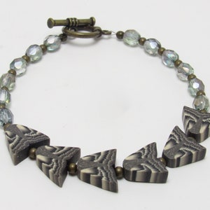 Op de afbeelding: Een ketting met een zilveren sluiting en een zilveren ketting. De ketting heeft een patroon van zwarte en witte pijlvormige kralen.