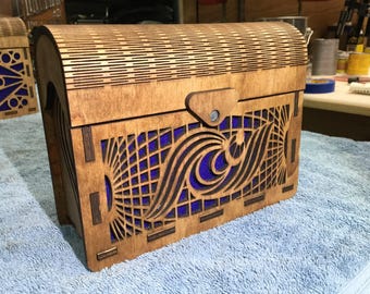 Puede incluir: Una caja de madera con tapa con bisagras y un diseño decorativo de olas recortado. La caja está teñida de un color marrón oscuro y tiene un fondo azul.