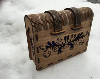 Puede incluir: Una caja de madera con tapa con bisagras y dos correas de cuero. La caja está decorada con un diseño floral azul y negro.