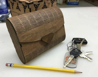 Puede incluir: Una caja de madera con un patrón decorativo y una tapa con bisagras. La caja está cerrada y tiene un acabado marrón. La caja está sobre una superficie blanca.