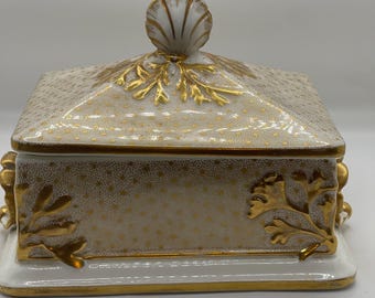 May include: A white porcelain box with a gold lid and gold accents. The lid has a shell design and the box has a floral design.