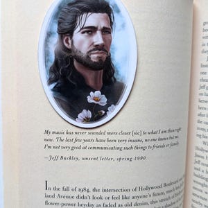 Könnte beinhalten: Ein ovales Lesezeichen mit einem Porträt eines Mannes mit langen, dunklen Haaren und Bart. Das Bild ist ein Gemälde mit einem weichen, künstlerischen Stil. Das Lesezeichen befindet sich auf einer Buchseite mit Text.
