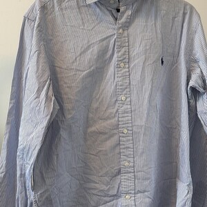 Peut inclure: Une chemise à manches longues à boutons, rayée bleu et blanc, avec un petit logo brodé sur la poitrine gauche.