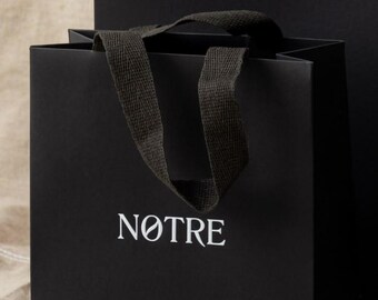 May include: A black shopping bag with black handles and the word "NOTRE" printed in white on the front.