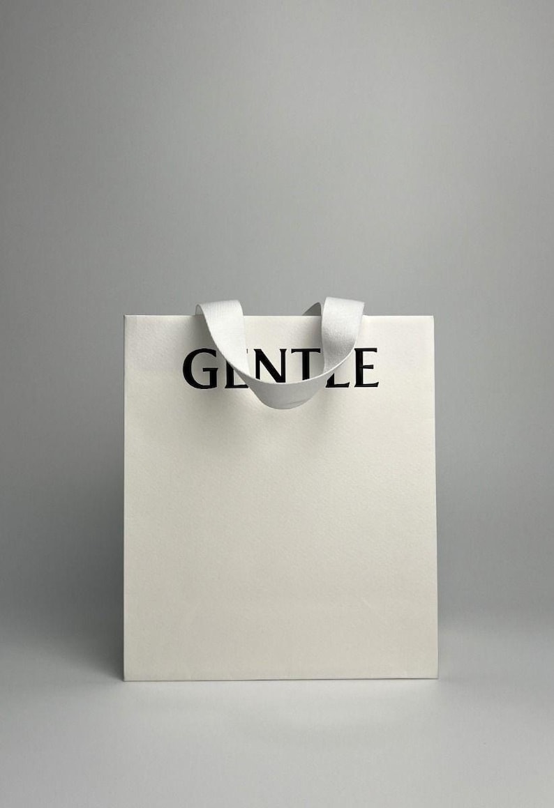 May include: White shopping bag with a white ribbon handle and the word "GENTLE" printed in black on the front.