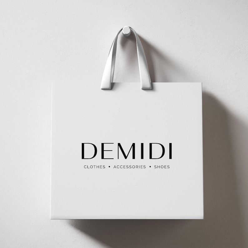 May include: White shopping bag with the brand name "DEMIDI" in black, and the words "CLOTHES &bull; ACCESSORIES &bull; SHOES" below. The bag has white handles and is hanging against a white wall.