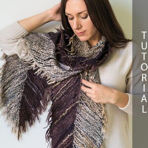 May include: A woman wearing a cream colored sweater with a brown, gray, and white fringed scarf. The scarf is tied in a loose knot at the neck.