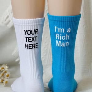 Könnte beinhalten: Ein Paar gerippte Crew-Socken, eine weiße und eine blaue. Die weiße Socke hat den gestickten Text "YOUR TEXT HERE" in Schwarz. Die blaue Socke hat den gestickten Text "I'm a Rich Man" in Weiß.