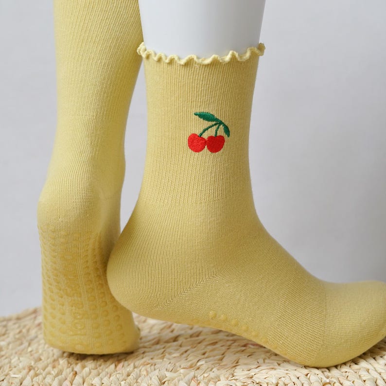 May include: A pair of yellow socks with a cherry embroidery design. The socks have a textured bottom for grip.