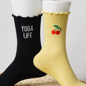 May include: A pair of black and yellow socks with grippy bottoms. One sock has the text "YOGA LIFE" embroidered on it, and the other has a red cherry embroidered on it.