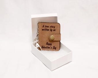 May include: A brown leather keychain with a small book charm. The book charm has the text "A love story written by us" and "Happy Valentine's Day" engraved on it. The keychain is in a white box.