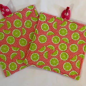 May include: Two pink and green pot holders with a lime pattern. The pot holders have a pink and white ribbon loop for hanging.