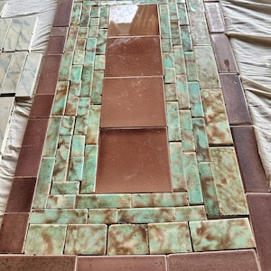 May include: An assortment of rectangular and square tiles in shades of brown and teal arranged in a rectangular pattern. The tiles have a glazed finish, creating a mosaic-like appearance. The arrangement suggests a decorative tabletop or wall feature.