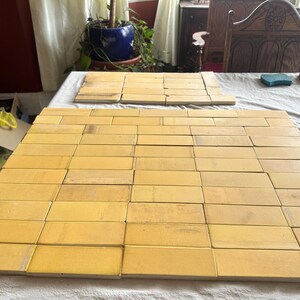 May include: A collection of rectangular, light yellow tiles arranged on a white surface. The tiles are laid out in a grid pattern, suggesting a potential flooring or wall covering project. The image is taken from an overhead perspective.