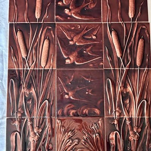 May include: A collection of brown ceramic tiles with embossed nature scenes. The tiles feature images of birds in flight, cattails, and aquatic plants. The tiles are arranged in a grid pattern, creating a cohesive design.