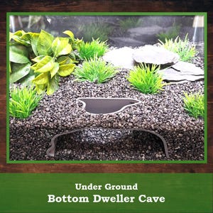 May include: An aquarium scene featuring a decorative cave, gravel substrate, and artificial plants. The cave is a dark grey, curved structure. The text "Under Ground Bottom Dweller Cave" is at the bottom of the image.