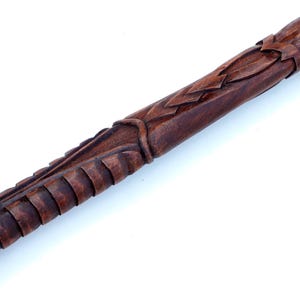 Puede incluir: Primer plano de un bast&oacute;n de madera con tallas intrincadas. El bast&oacute;n es de color marr&oacute;n oscuro y tiene un acabado liso y pulido.