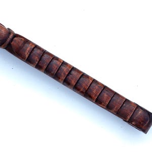 Puede incluir: Primer plano de un bast&oacute;n de madera con un mango tallado y texturizado. El mango es de color marr&oacute;n oscuro y tiene una serie de crestas elevadas.