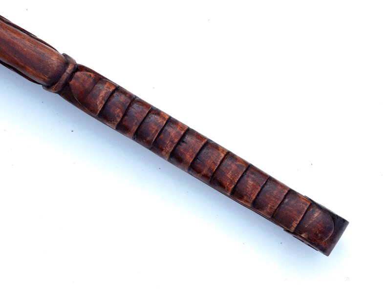 Puede incluir: Primer plano de un bast&oacute;n de madera con un mango tallado y texturizado. El mango es de color marr&oacute;n oscuro y tiene una serie de crestas elevadas.