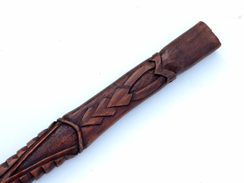 Puede incluir: Primer plano de un bast&oacute;n de madera con tallas intrincadas. El bast&oacute;n es de color marr&oacute;n oscuro y tiene un acabado liso y pulido.