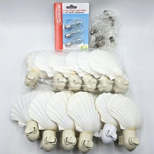 May include: A collection of white seashell-shaped night lights with on/off switches, packaged in clear plastic. Also included are three clear night light bulbs in a Sunbeam package and a separate bag of clear bulbs.