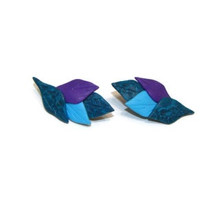 Op de afbeelding: Een paar oorbellen met drie gelaagde bladeren in tinten teal, blauw en paars.